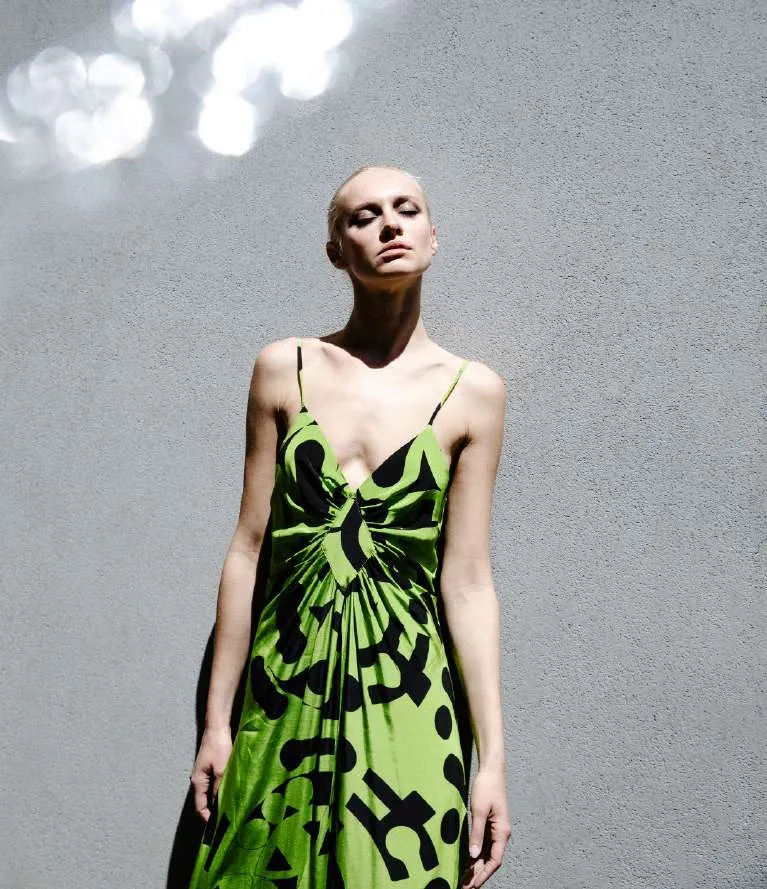 Model in a green and black printed slip dress against a pale grey wall