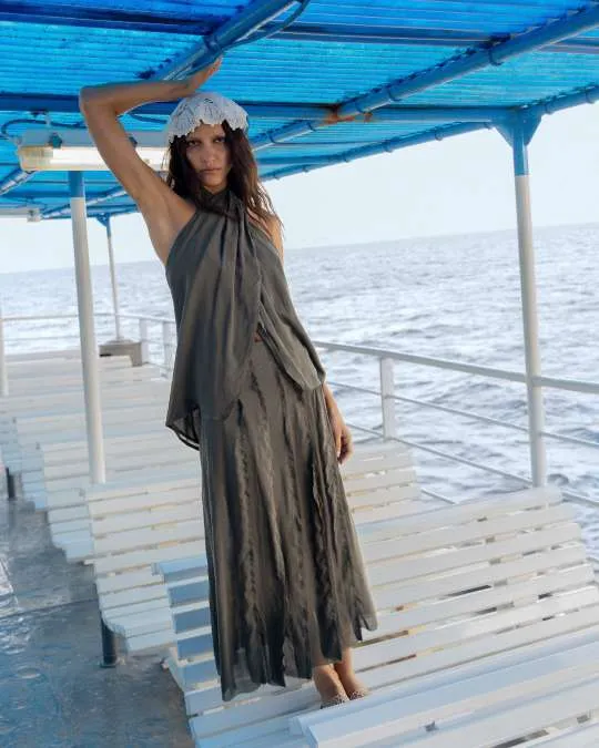 Model in an olive draped halter top and long skirt with a white crochet headscarf, on the shaded deck of a boat