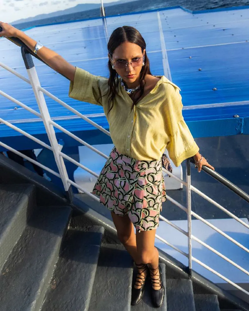 Model in a yellow shirt and pink and green heart-print shorts on a ferry staircase