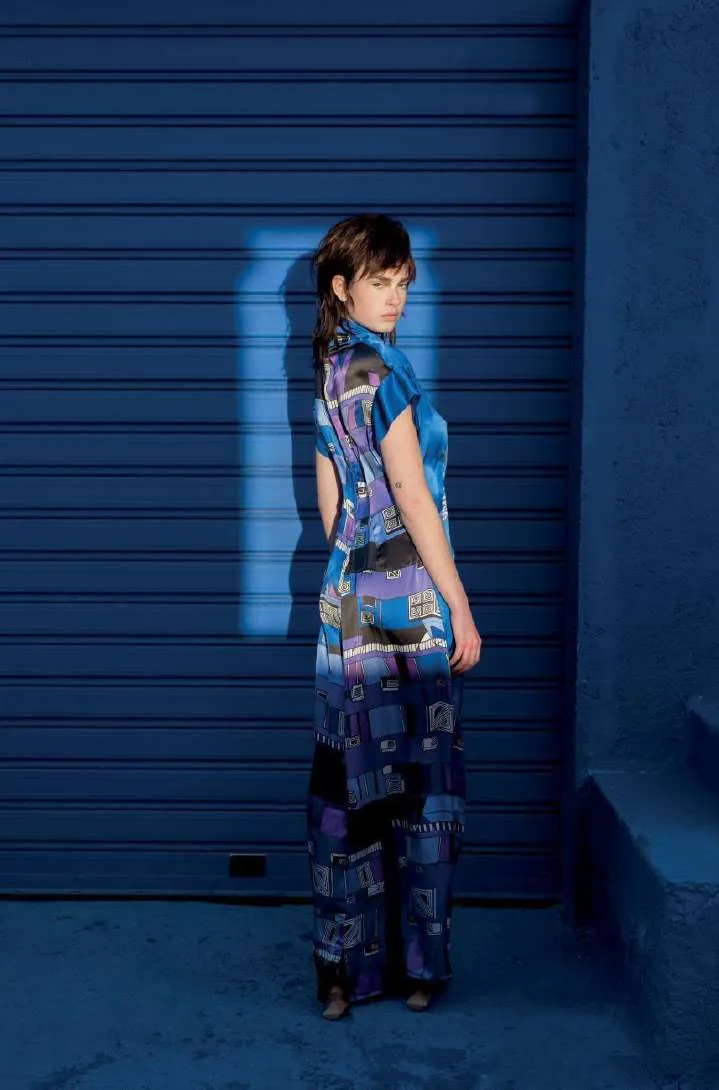 Model seen from behind in the No Signal dress, blue and purple printed silk, in front of a blue roller shutter