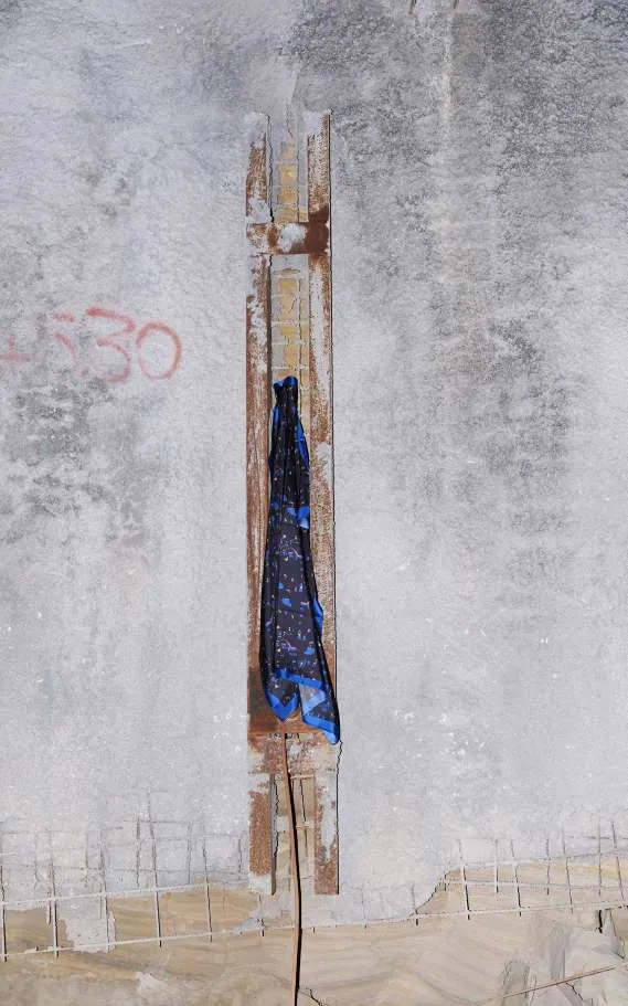 A navy scarf with blue marks hung in a groove of a concrete wall
