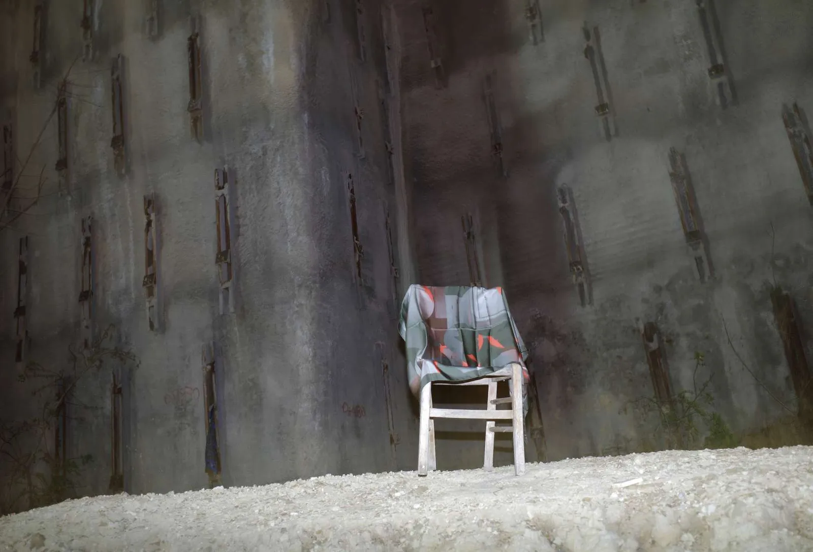 The Out of Sequence scarf, grey with orange, draped over a white chair in front of a concrete retaining wall