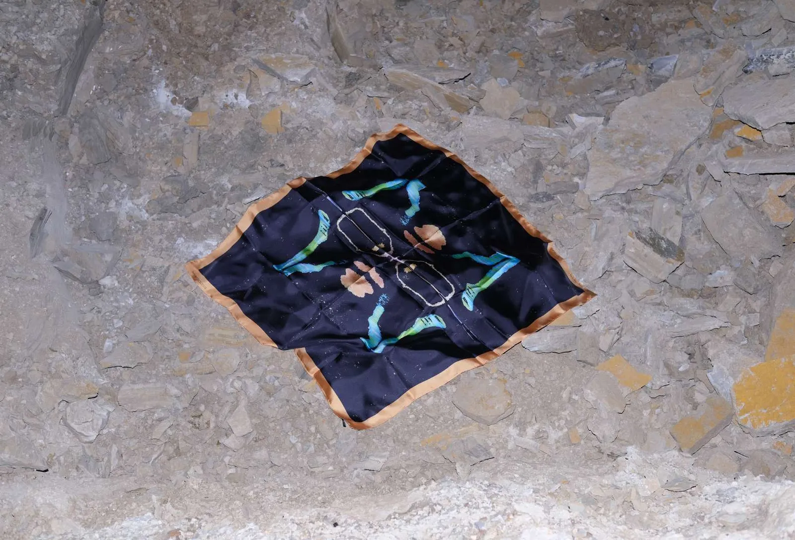 The Run scarf, black with cyan and peach shapes and a peach border, laid on white rubble