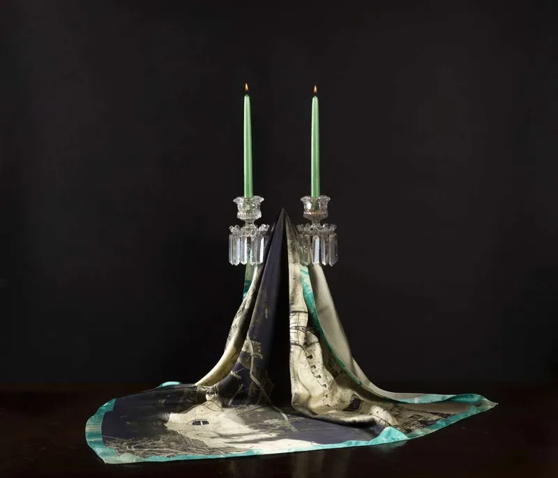 Still life on black: the Prastos scarf, beige and black, draped between two glass candlesticks with green candles