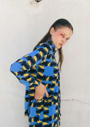 Model in a blue, black and yellow printed shirt and matching trousers against a white wall