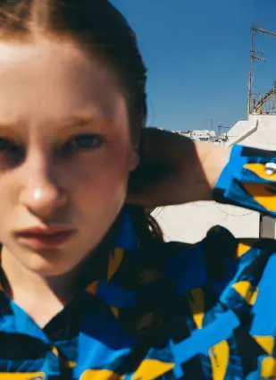 Close-up of a model in a blue, black and yellow block-print shirt, one hand behind her head