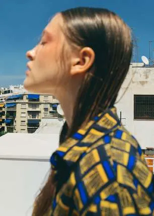 Model in profile in a yellow, navy and blue geometric-print shirt on a city rooftop