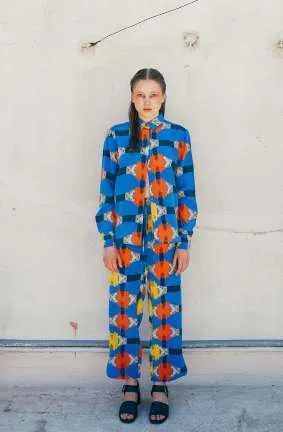 Model in a blue shirt and trousers with an orange and yellow print, against a white wall