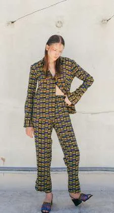 Model in an olive and yellow check-print shirt and trousers, against a white wall