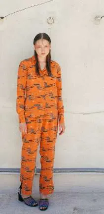 Model in an orange shirt and trousers with a navy and grey print, against a white wall
