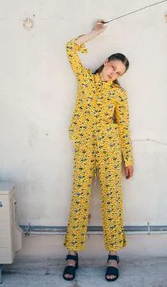Model in a yellow shirt and trousers with a small grey print, against a white wall