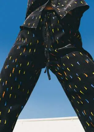 Black trousers with a multicoloured dash print, seen from below against a blue sky